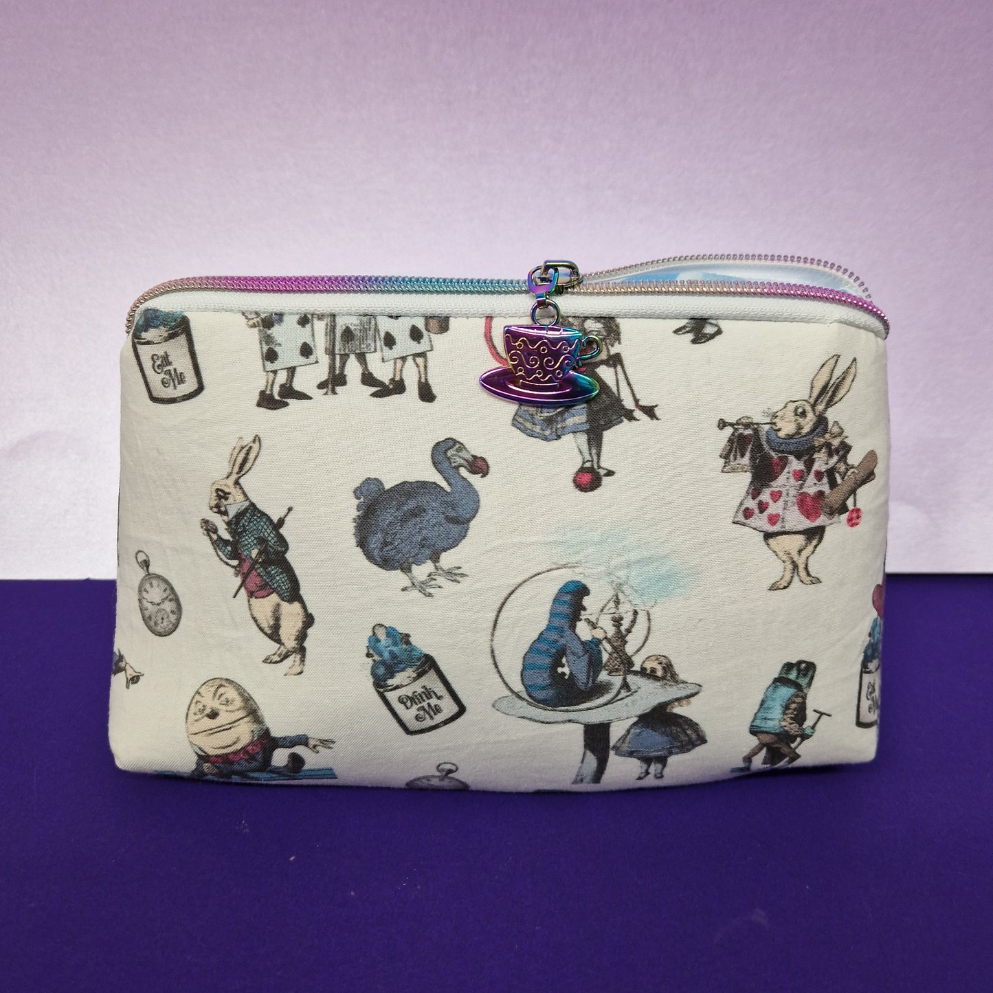 Wonderland lined triangle cosmetic bag with rainbow tea cup zipper pull